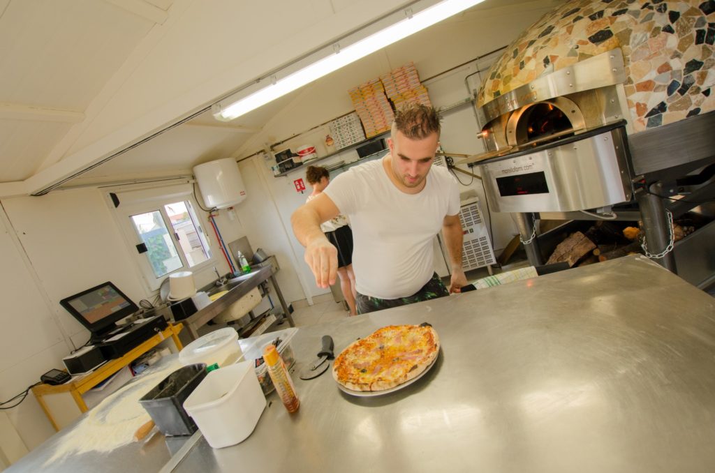 Pizzaïolo préparant une pizza devant le four à bois en mosaïque